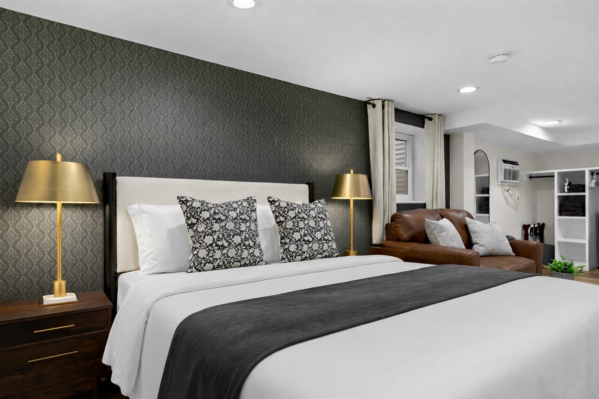 Spacious studio bedroom with a plush king bed, elegant lighting, and cozy seating—blending comfort and style for a restful, inviting stay.