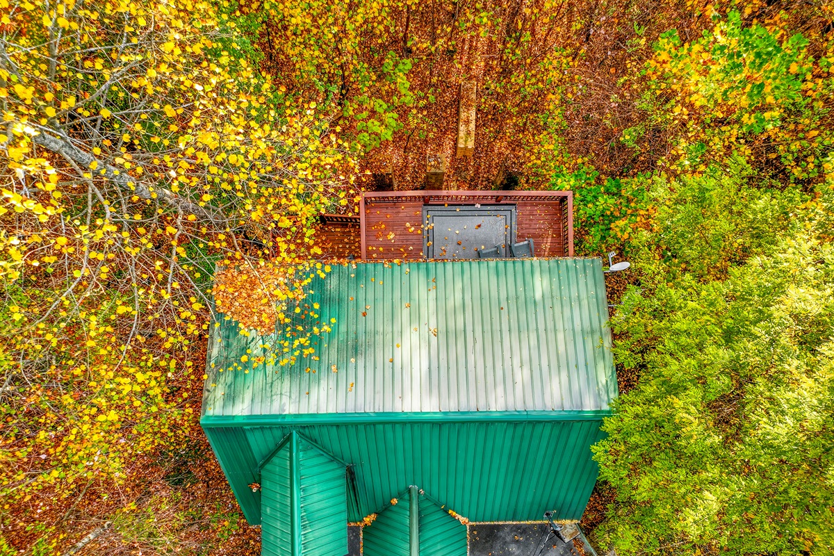 An aerial view of a serene autumn landscape, where vibrant hues of gold, orange, and red blanket the forest. Cozy cabins nestle among the trees, with majestic mountains rising in the distance.