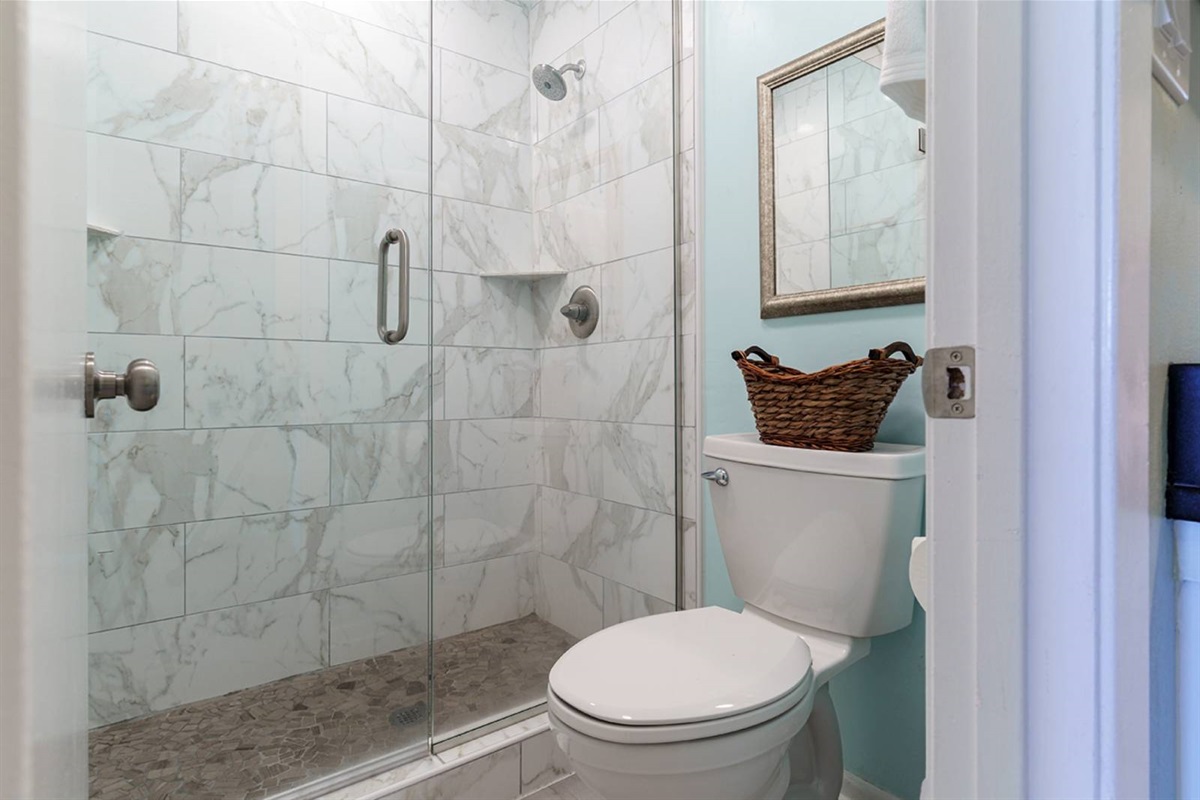 Spa-worthy shower in the master bath. Marble tile walls, pebble stone floor, and a frameless glass enclosure — a cut above most rentals.