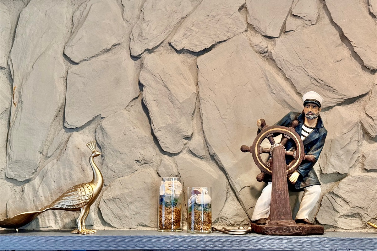 Above it, a mantel shelf displays beachy, nautical-inspired décor—from a vintage ship captain figurine at the helm to golden seashell accents and elegant birds.