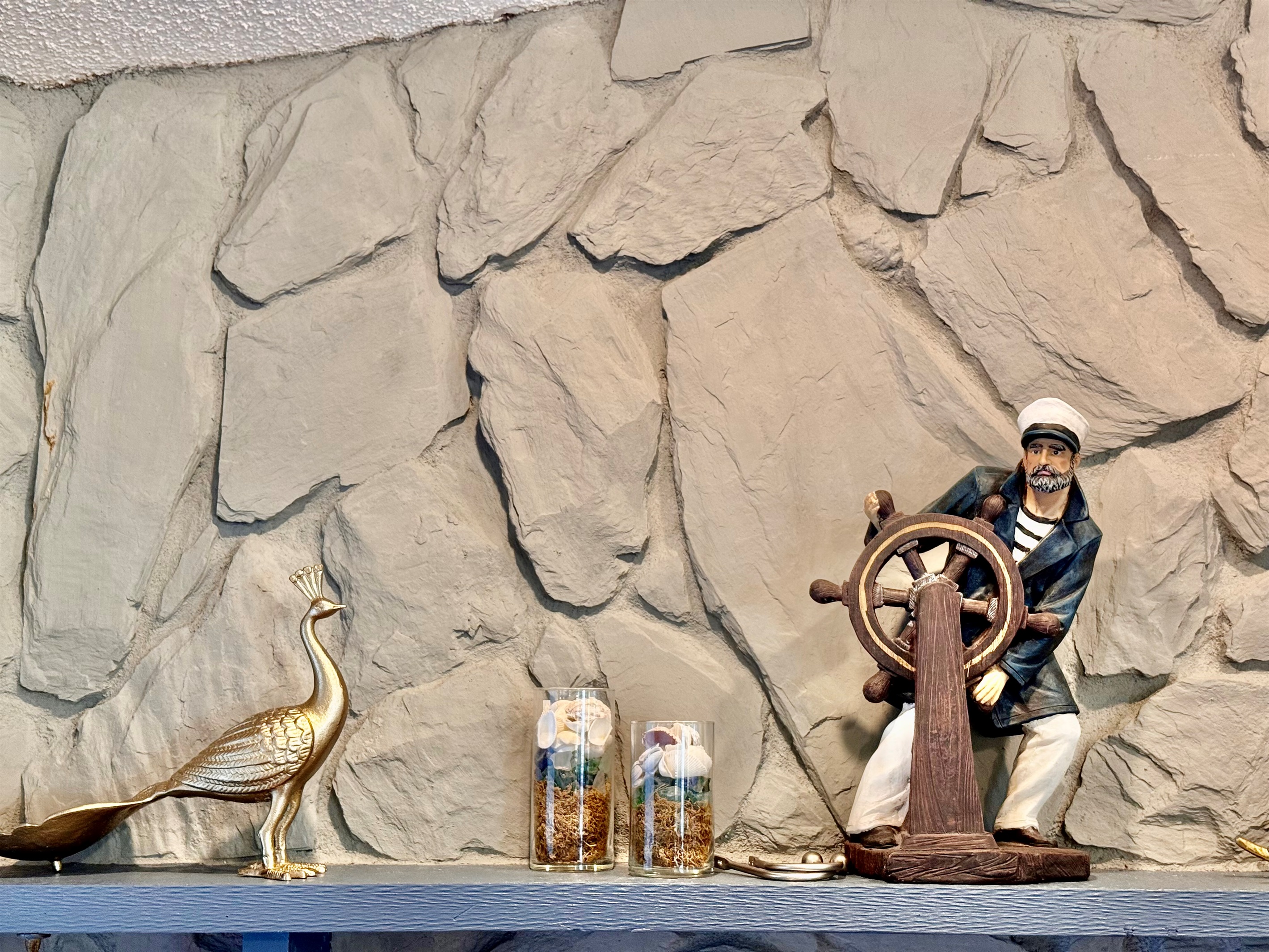 Above it, a mantel shelf displays beachy, nautical-inspired décor—from a vintage ship captain figurine at the helm to golden seashell accents and elegant birds.