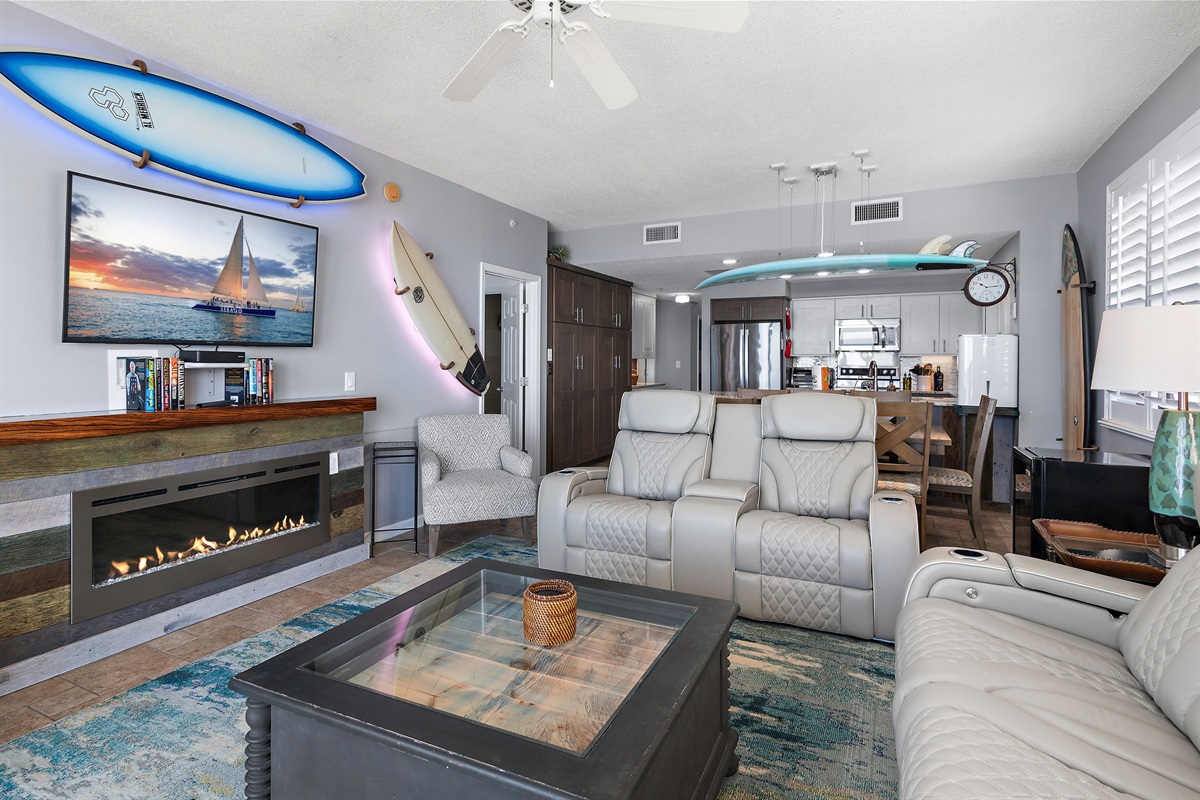 The Gulf View Living Room features a large Smart TV, electric fireplace, backlit surfboard decor, and brand new, leather reclining sofa and loveseat!