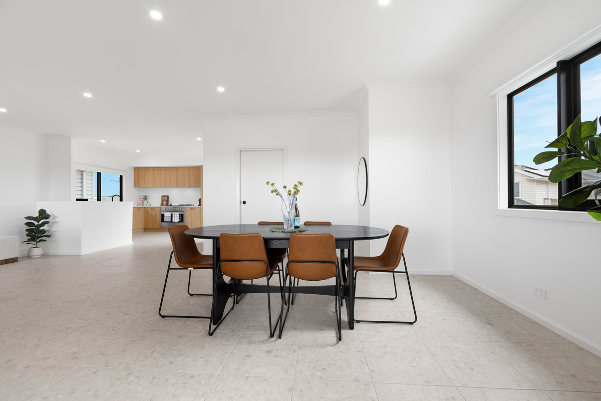 Dining table and chairs in the open-plan space, with the kitchen in the background and a large window for natural light.