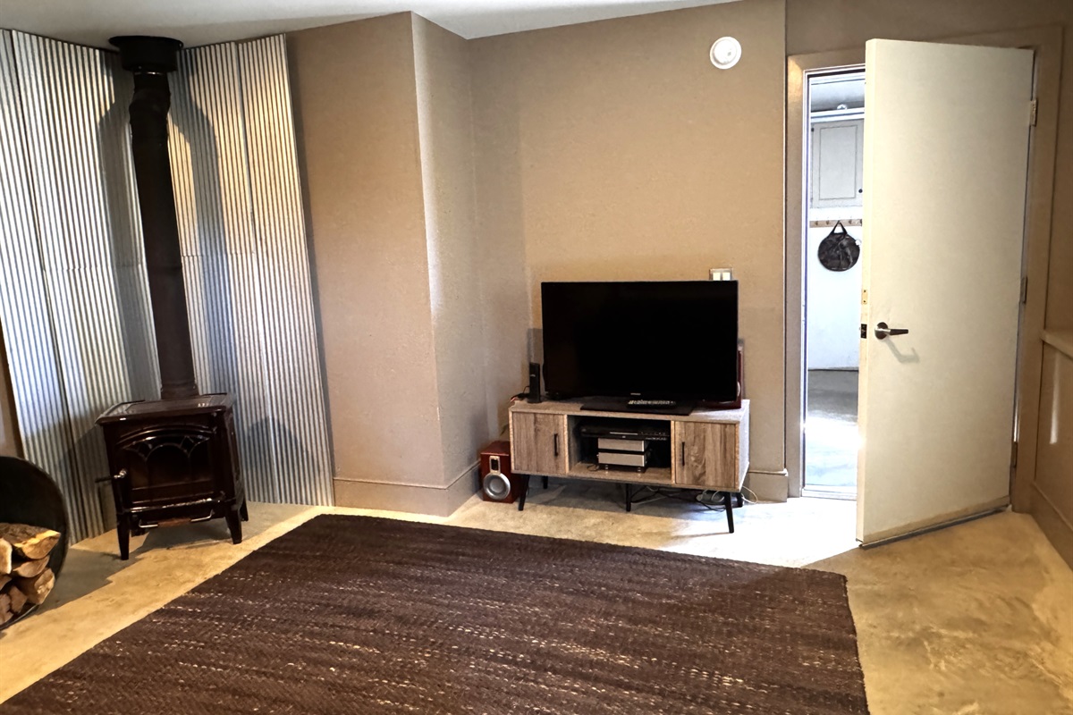 The home’s primary media room located on the lower level, featuring a smart Roku TV and cozy lounge area. This dedicated social space offers a quiet retreat for movie nights, positioned conveniently between the guest bedroom and the private garage.