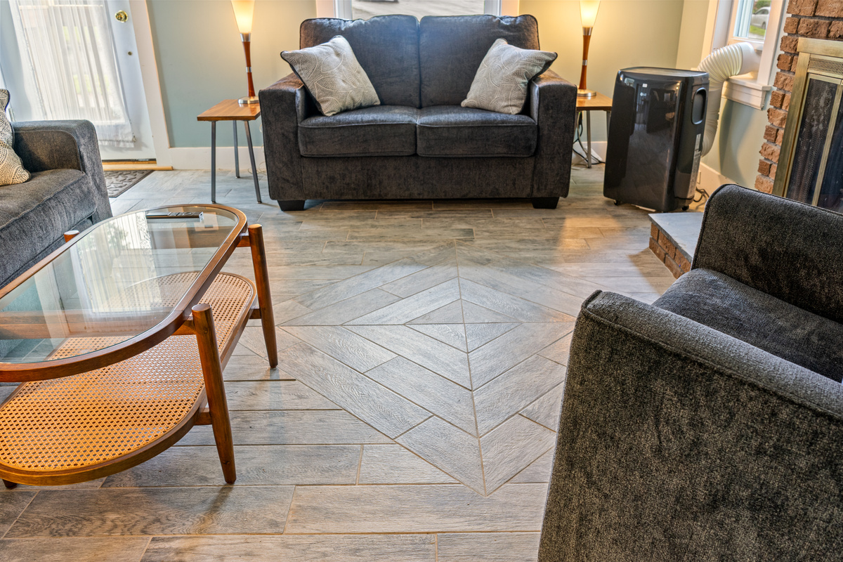 A lower perspective highlights the living room's custom diamond shape floor pattern. This view details the surrounding seating arrangement and a provided portable AC unit for reliable indoor cooling during warmer summer months.