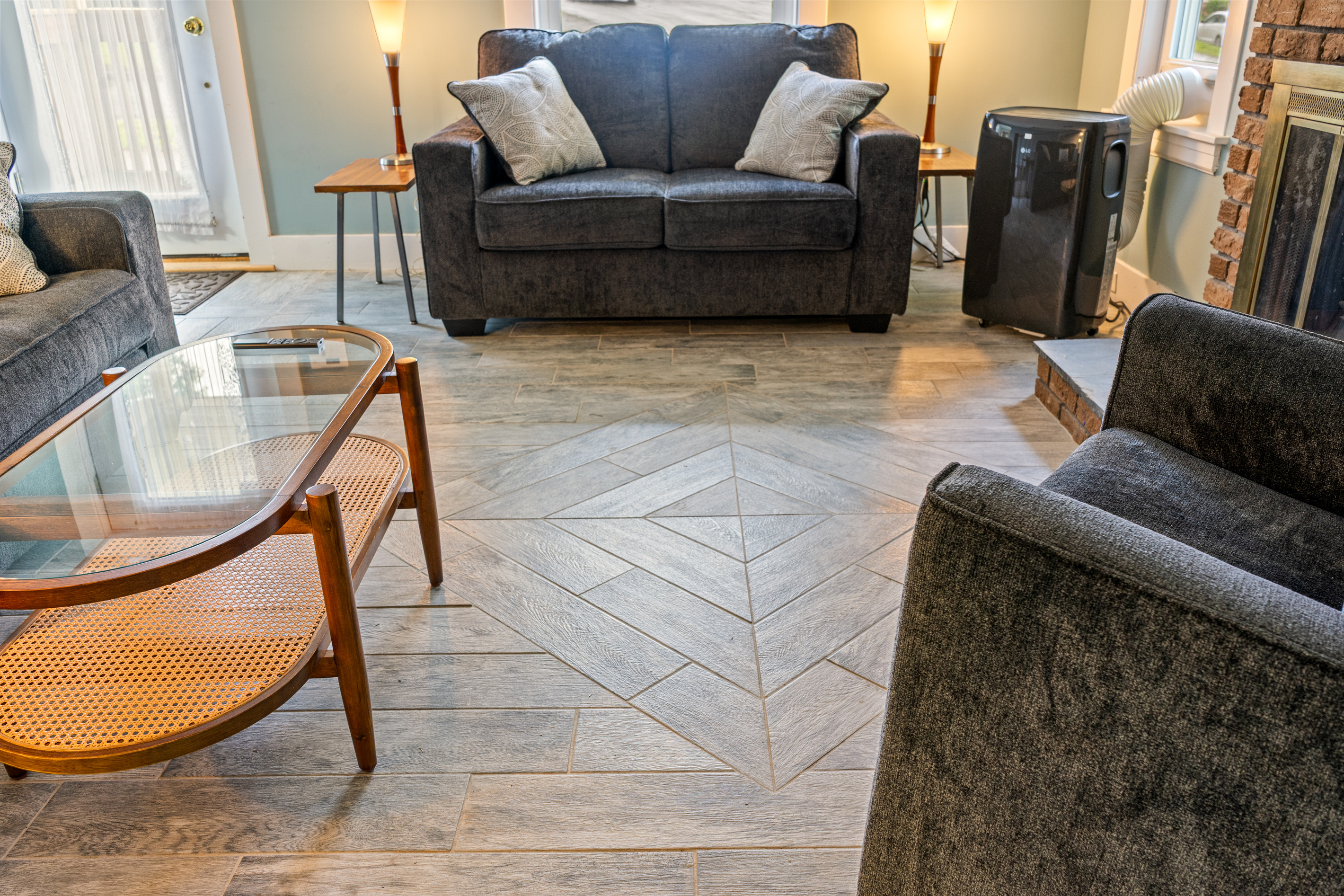 A lower perspective highlights the living room's custom diamond shape floor pattern. This view details the surrounding seating arrangement and a provided portable AC unit for reliable indoor cooling during warmer summer months.