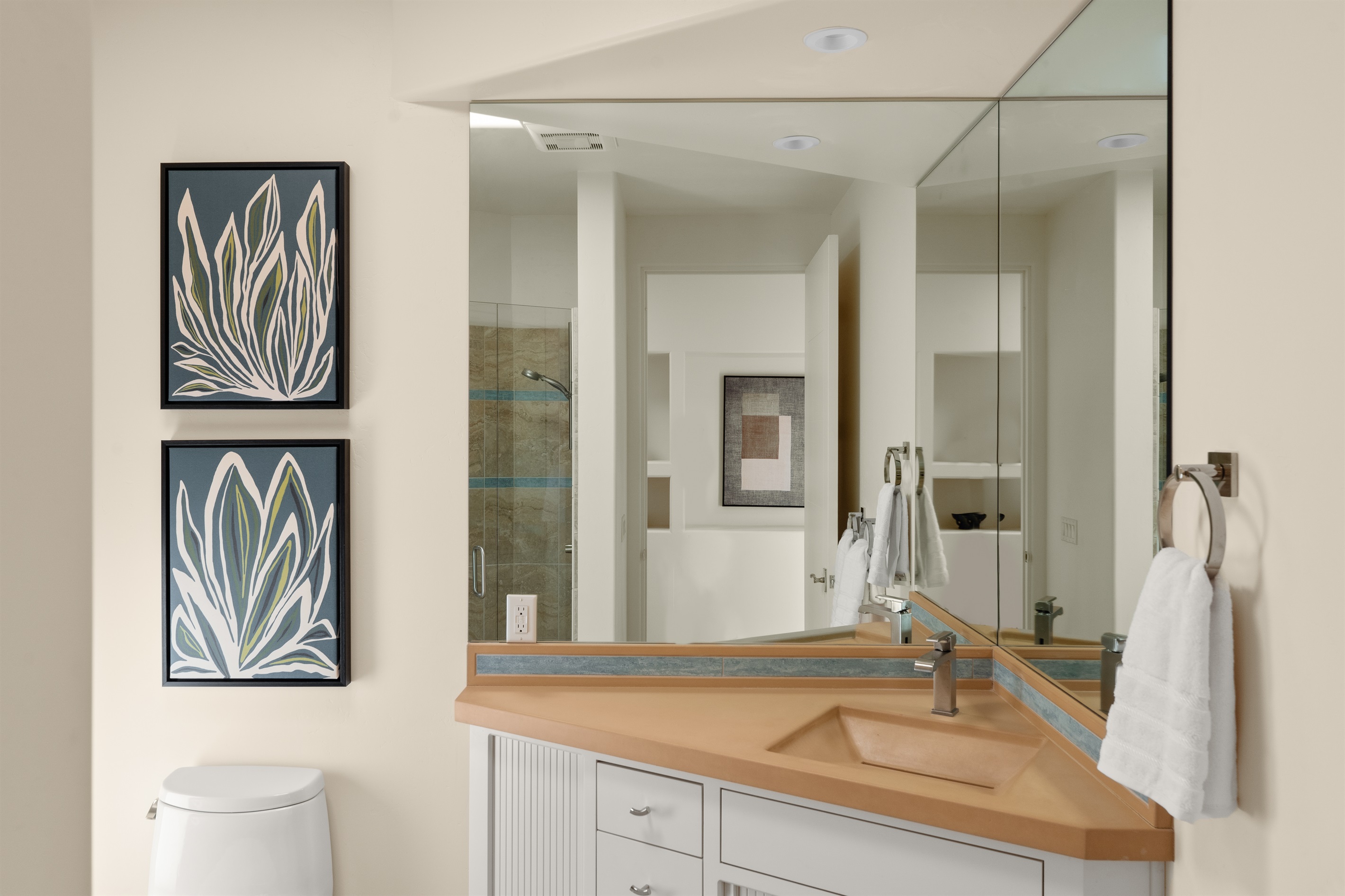 This bright and inviting guest bathroom features desert-inspired artwork, custom earth-toned countertops, and a spacious walk-in shower.