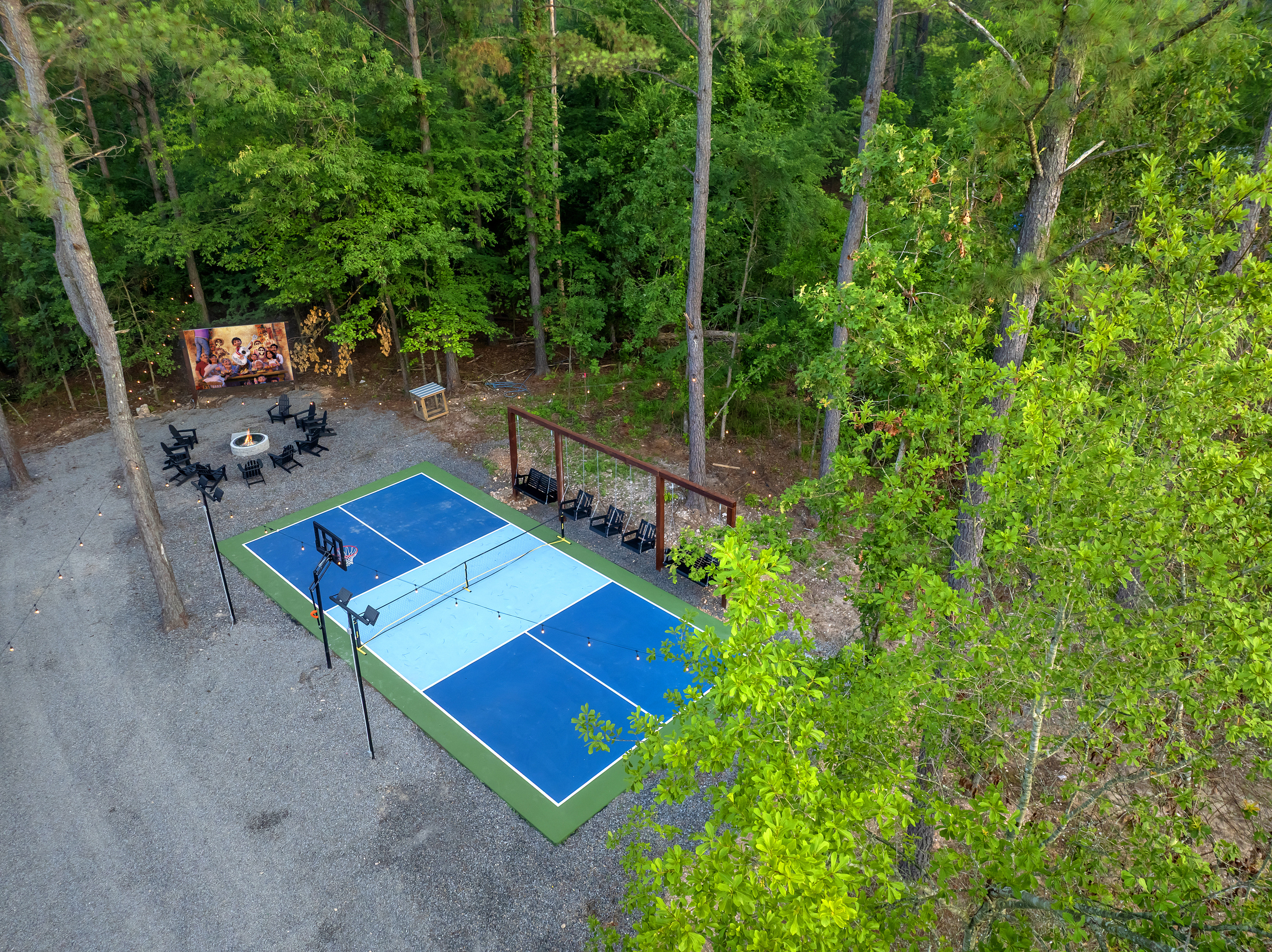Private pickleball + basketball court surrounded by towering pines, with spectator swings, a fire pit & outdoor cinema just steps away at the firepit. Play all day, movie night after dark.