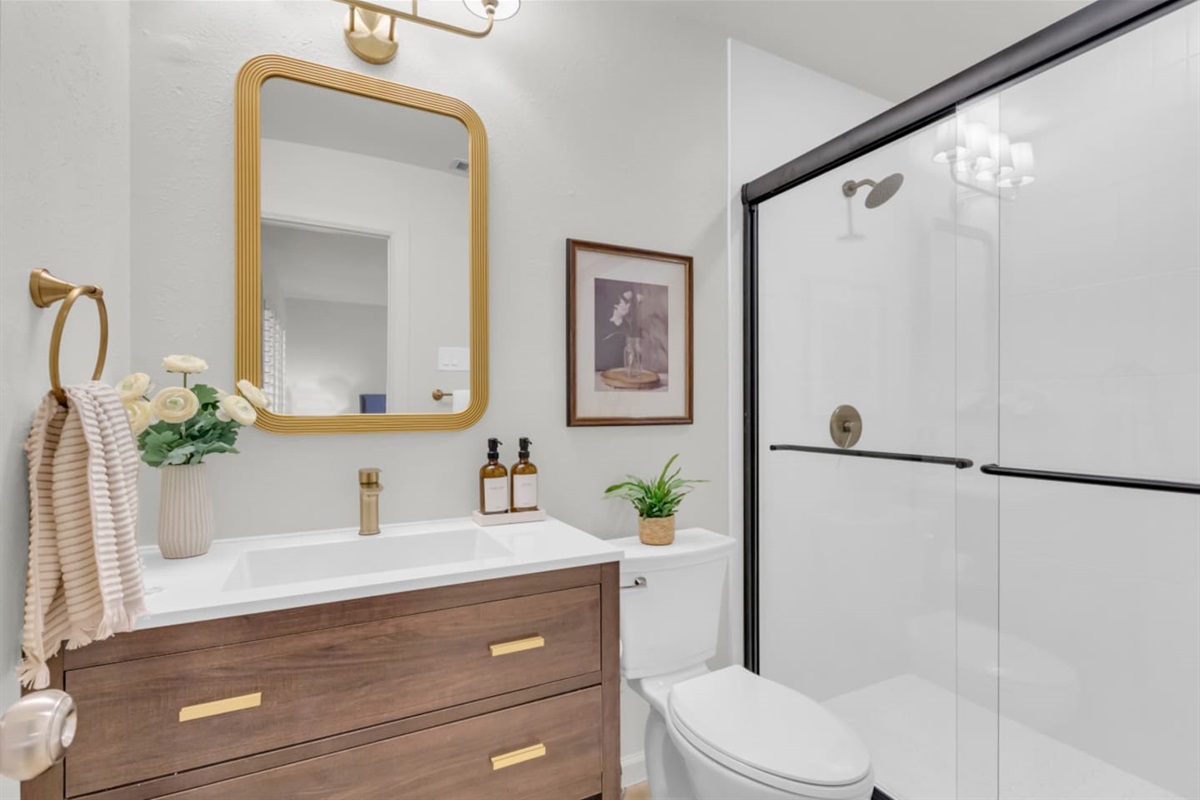 Updated bathroom with walk-in shower, gold accents, and Ginger Lily Farms toiletry set. Fresh towels and essentials ready for your stay.