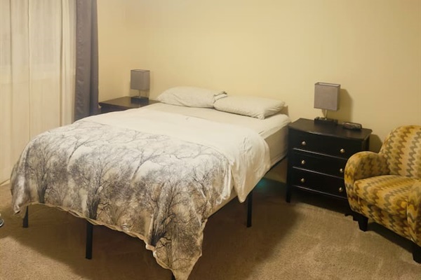 Cozy carpeted bedroom with comfy bed, dual nightstands, and accent chair