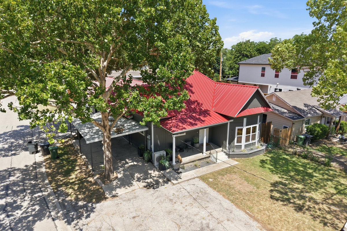 Charming home with vibrant red roof, shady trees, and inviting outdoor space awaits!