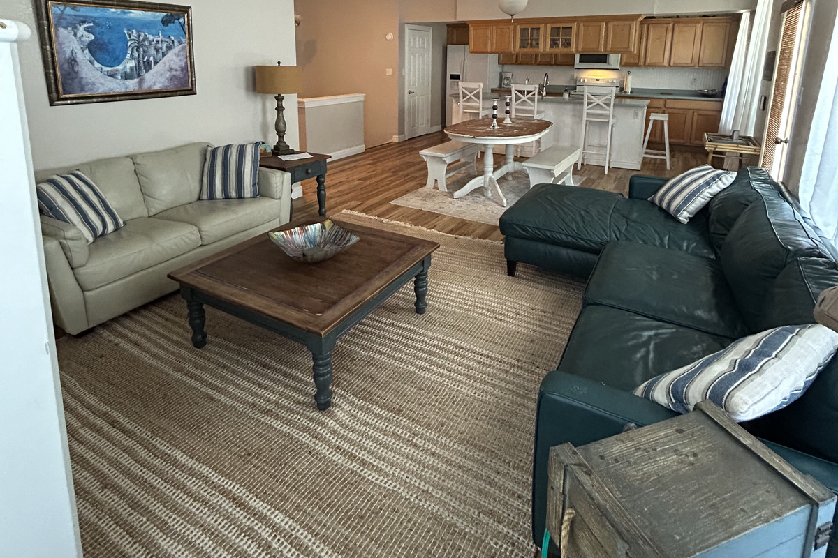 Bright and airy open-concept living space with vaulted ceilings and coastal charm. Relax on plush seating with nautical-inspired accents, enjoy natural light from multiple windows, and take in views of the kitchen and dining areas. 