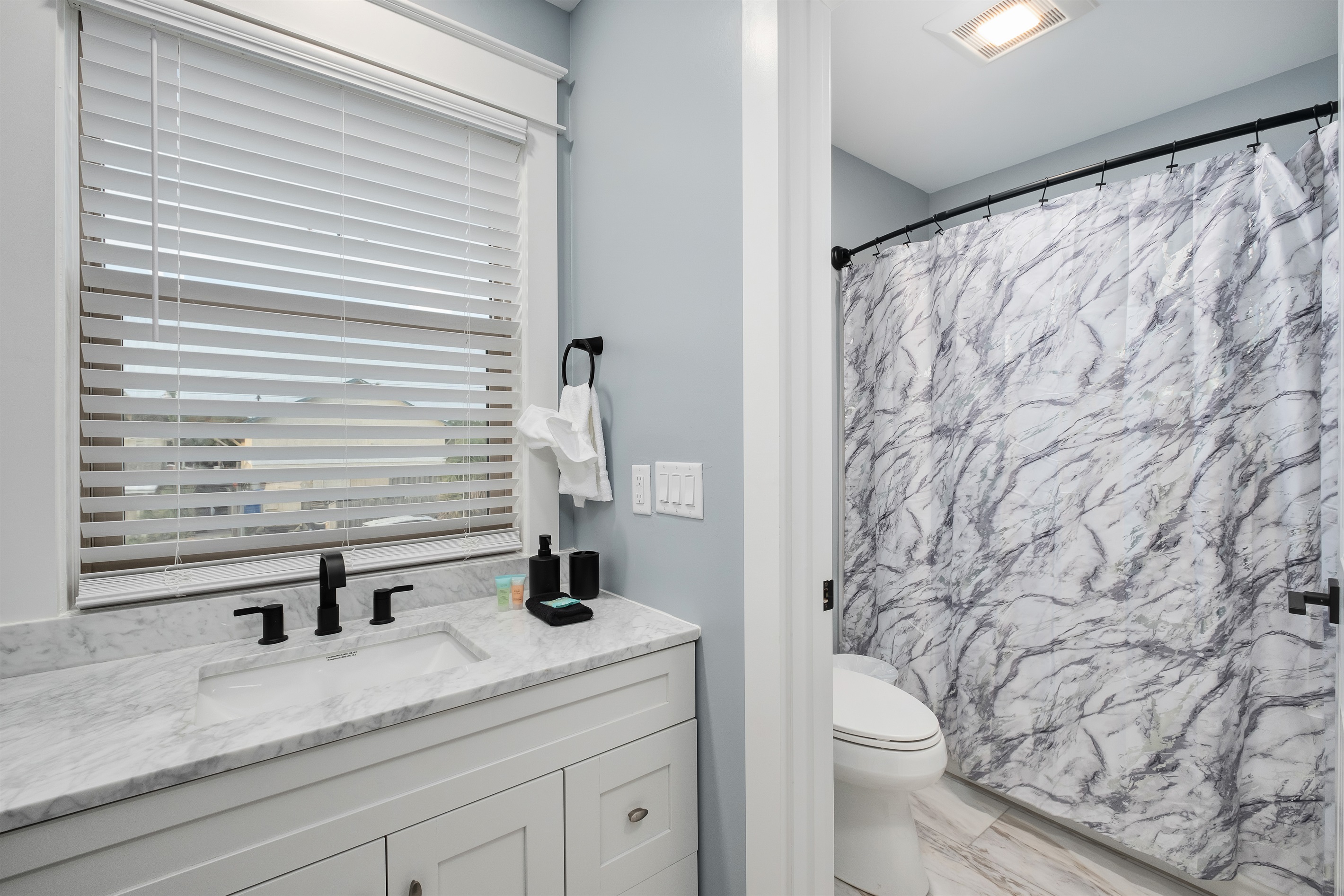 Indulge in the luxury of this beautifully designed bathroom featuring high-end fixtures, a marble countertop, and a sophisticated marble shower curtain. Ideal for a relaxing and rejuvenating experience.