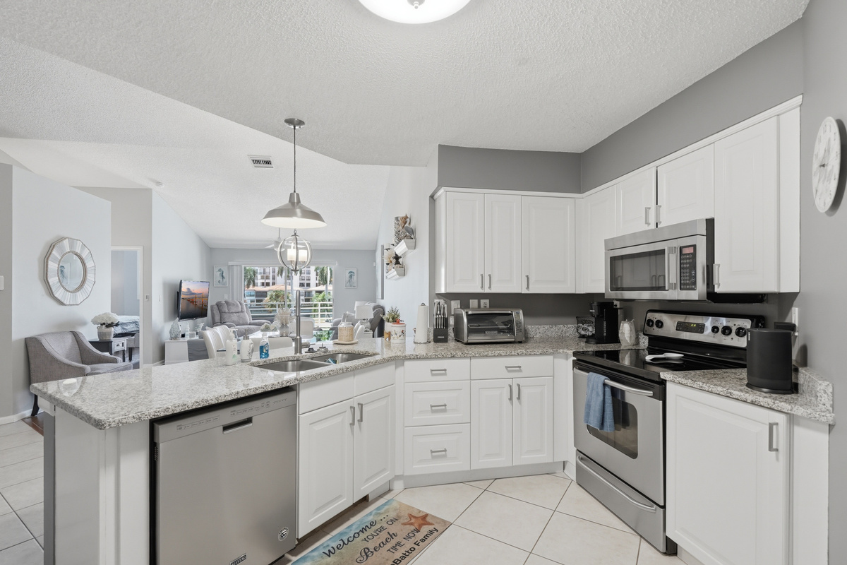 The fully equipped kitchen features stone countertops, solid wood cabinets, and modern appliances, including a refrigerator, range/oven, microwave, dishwasher, and garbage disposal. Everything you need to prepare meals.
