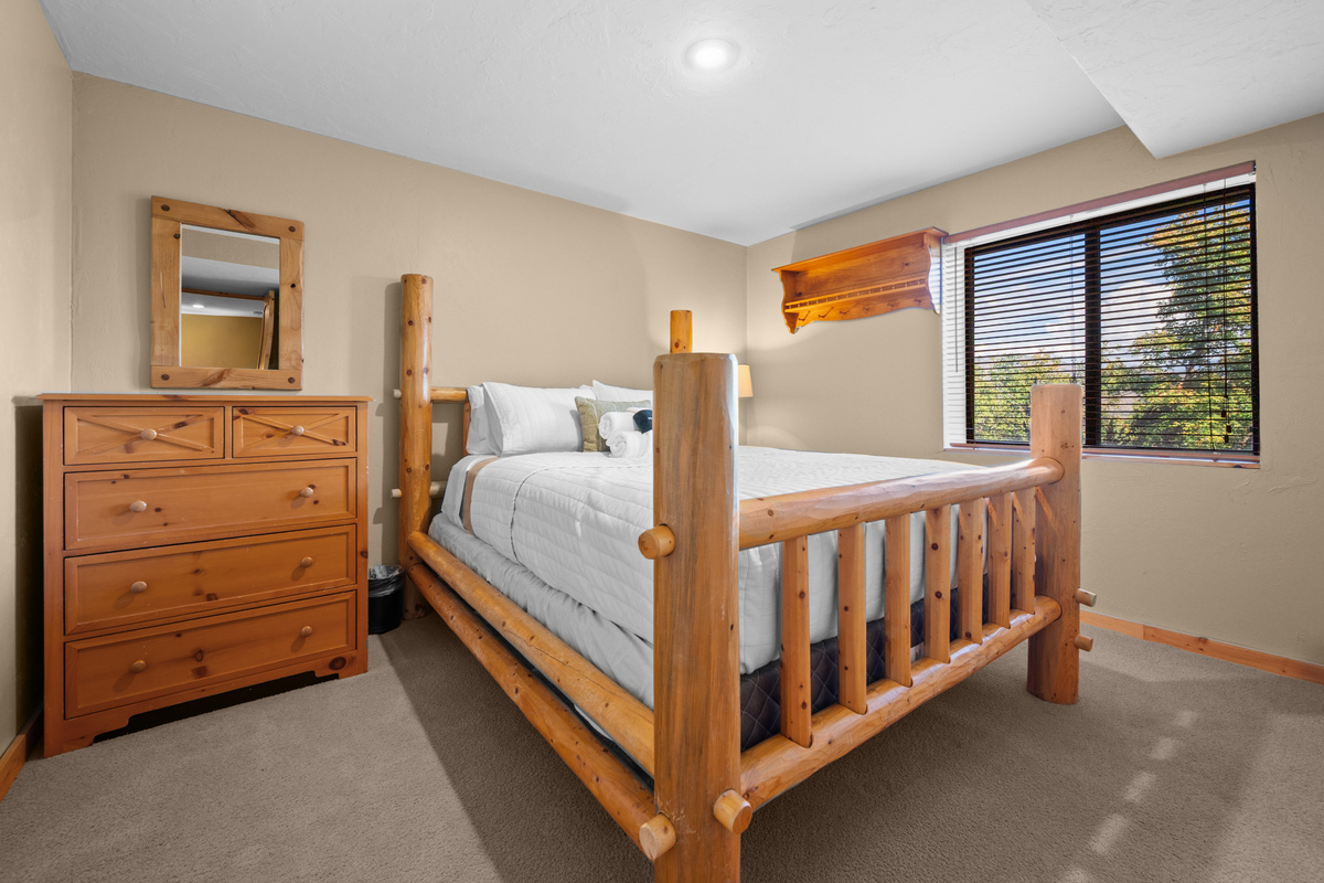Downstairs queen bedroom with rustic log-frame bed and plenty of natural light.