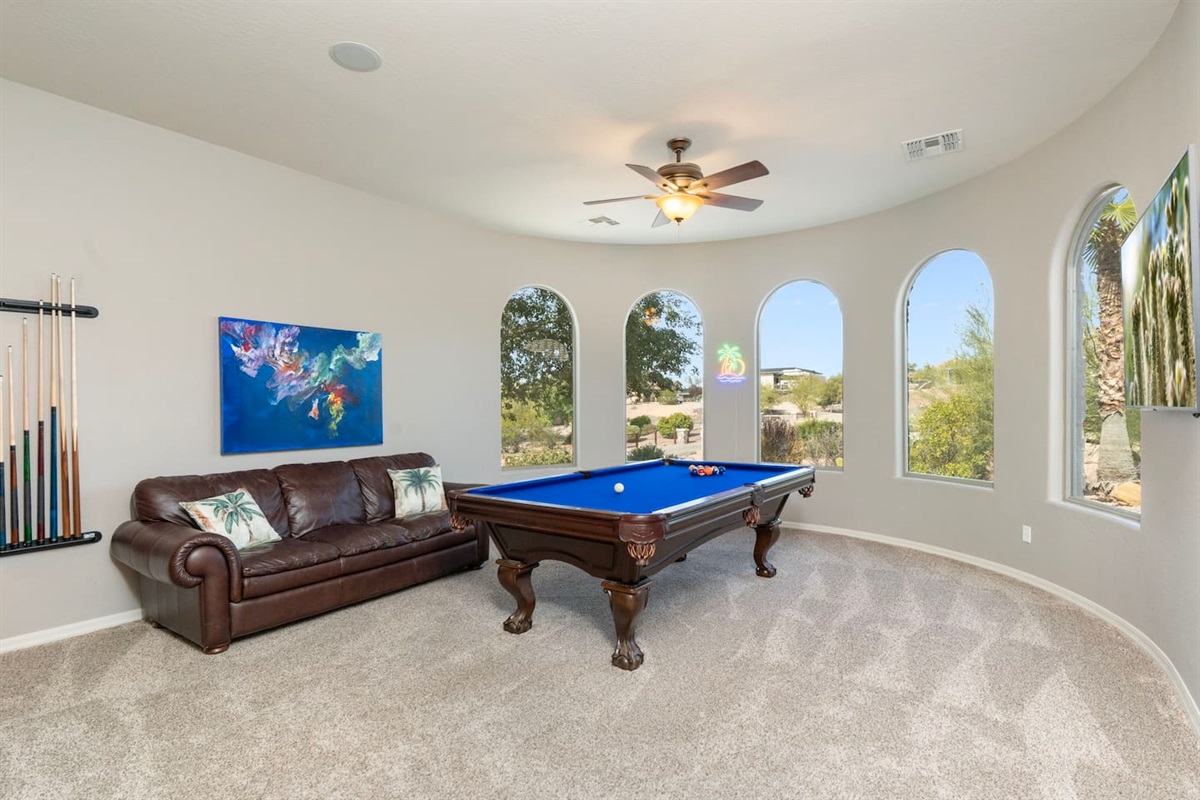 Game room featuring the leather couch, a full-size pool table, and large arched windows with scenic views.