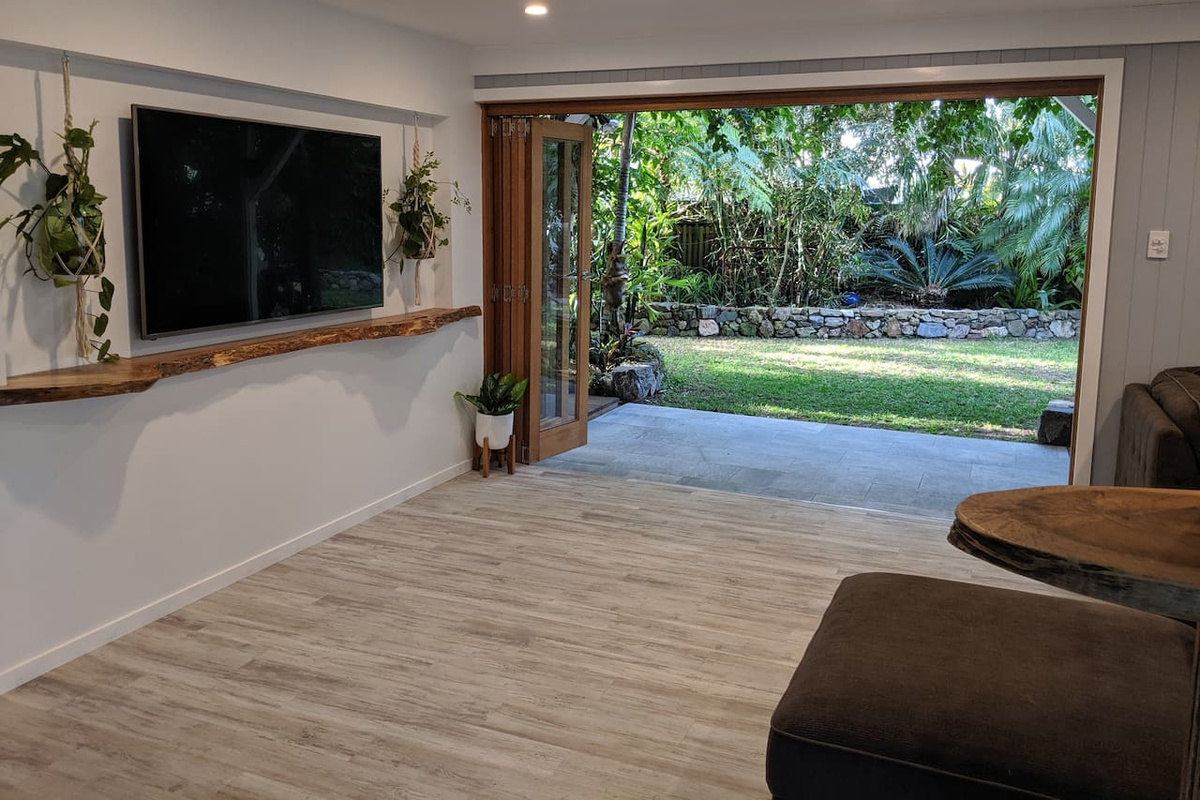A wall-mounted TV, casual seating and wide-opening doors make this living area at Aaron's Beachside Boat House a practical part of the lower-level layout.