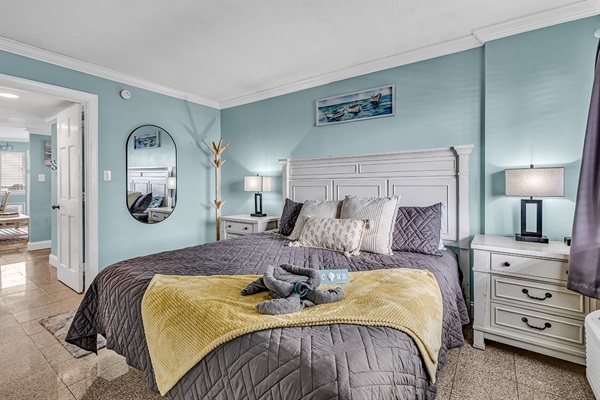 King bedroom with plush bedding, nightstands with lamps, dresser with mirror, and coastal blue décor