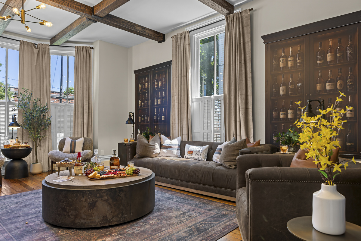 The main living room sets the tone with exposed wood beams, a striking bourbon display cabinet, and comfortable leather seating for the whole group.