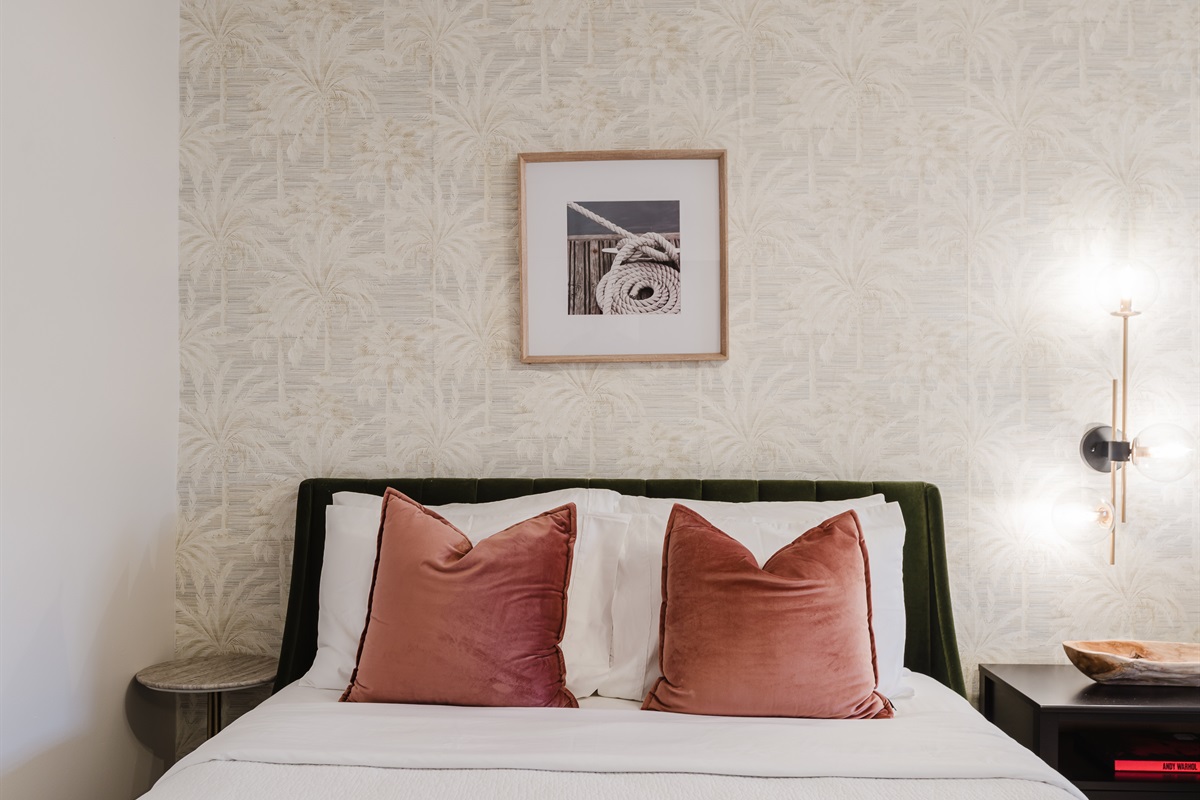 Bright coastal suite with two queen beds, private ensuite bath, smart TV, blackout bamboo shades, and a rattan ceiling fan—ideal for families or shared stays.