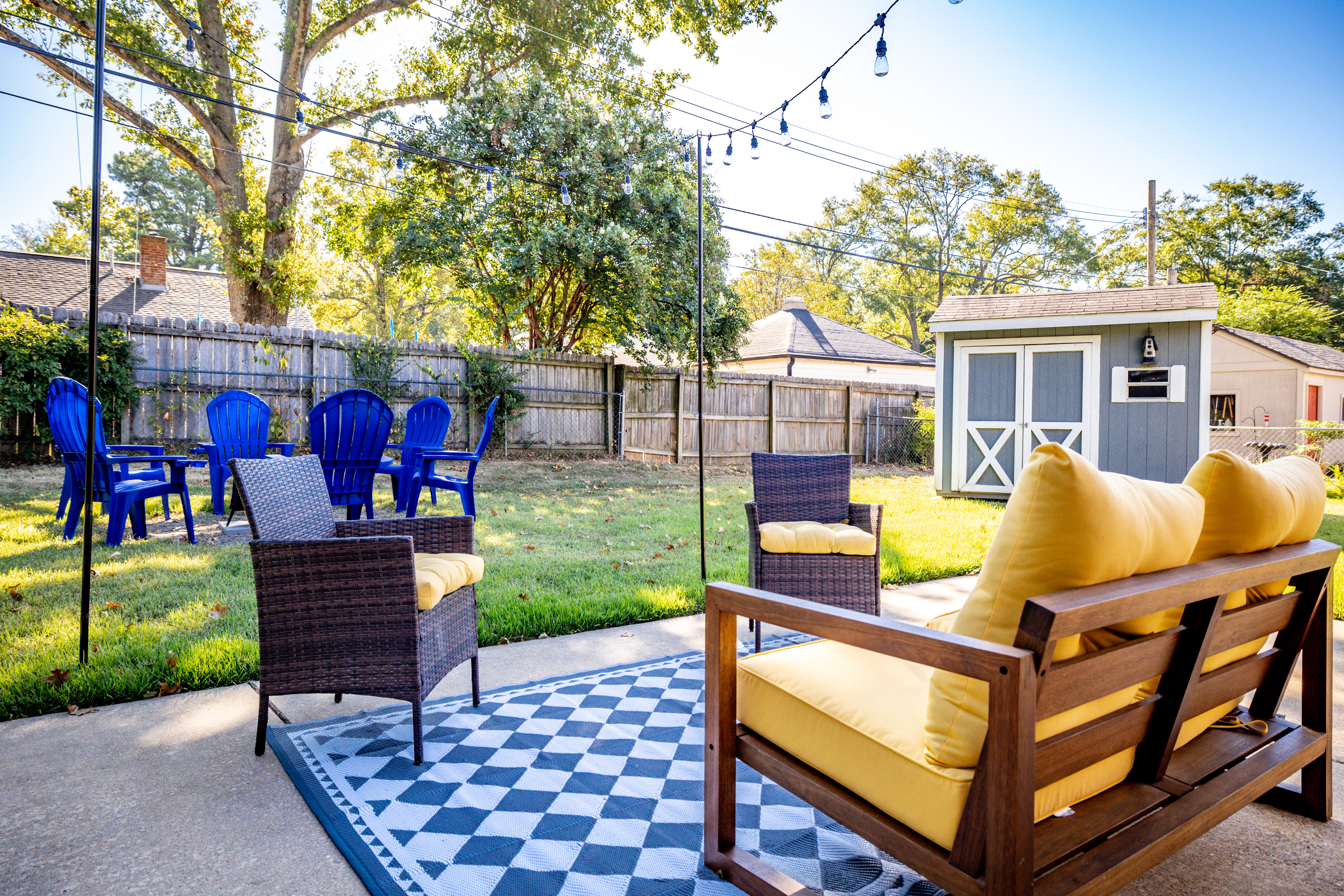 Fenced backyard with string-lit patio, fire pit, and electric grill.