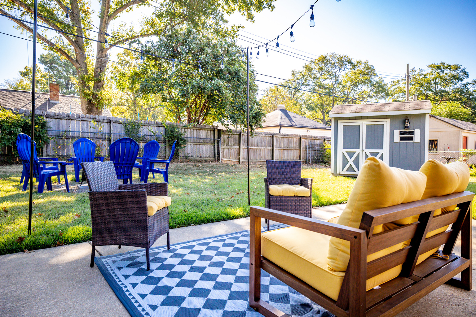 Fenced backyard with string-lit patio, fire pit, and electric grill.