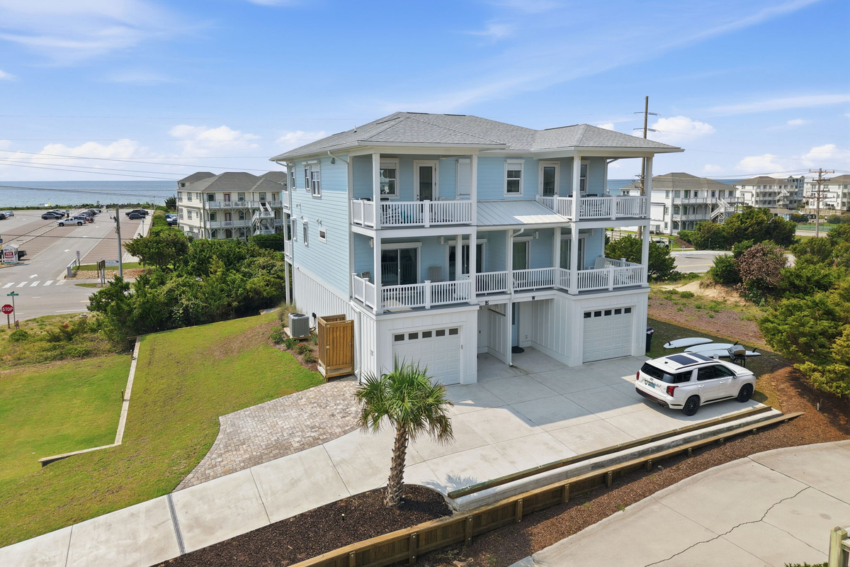 Aerial view of the property highlighting the large home layout, balconies, garage spaces, and surrounding beach community