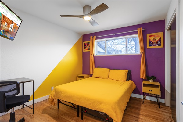 A room strikingly decorated in purple and yellow, equipped with a TV and study table for both entertainment and productive sessions.