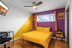 A room strikingly decorated in purple and yellow, equipped with a TV and study table for both entertainment and productive sessions.