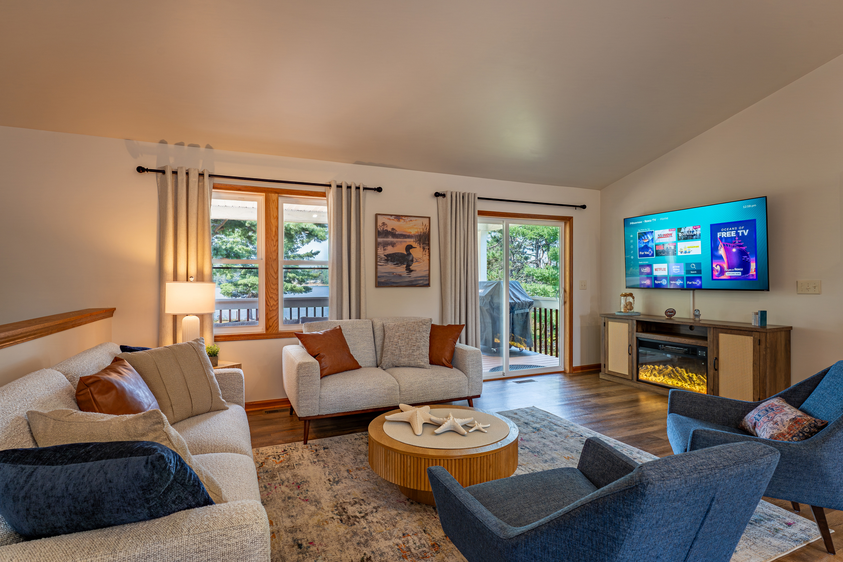 Open-concept main living area with lake views, fireplace, 70" Roku TV, and seating for the whole group