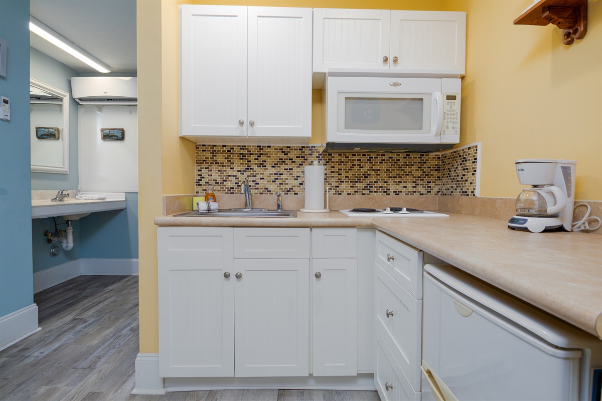 Compact kitchenette with white cabinetry, microwave, mini fridge, and coffee maker&mdash;perfect for quick meals and easy mornings