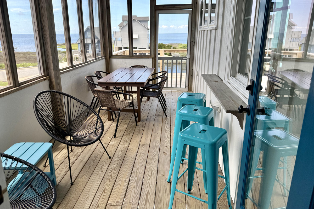 New table and chairs on the screen porch. Pass through window from the inner bar.