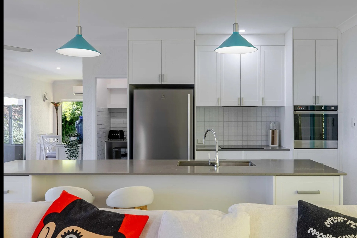 The kitchen includes a wide island bench, full-size fridge, oven and cooktop, with open connection to the lounge and dining areas.