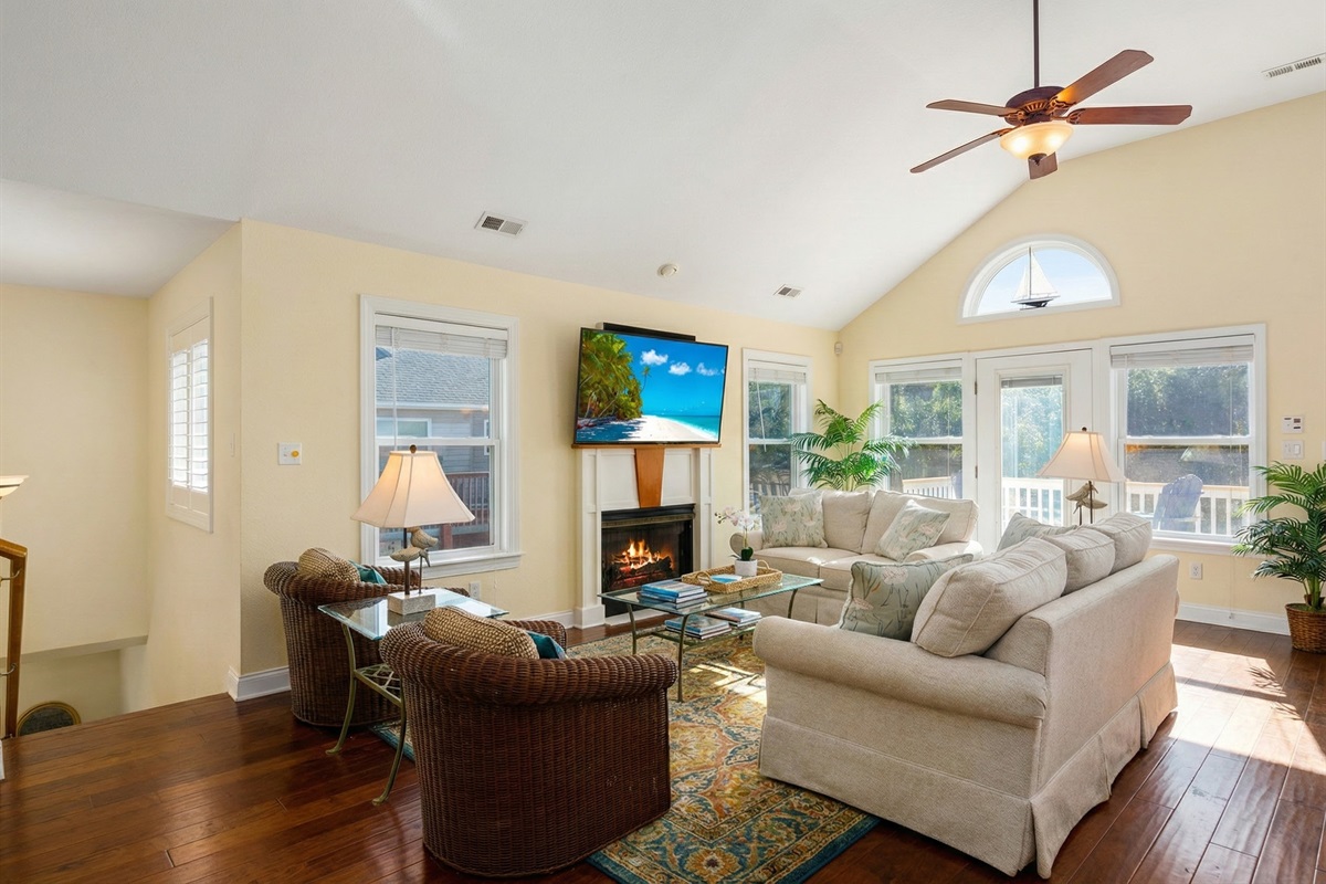 The airy main living room featuring vaulted ceilings, a cozy fireplace with a mounted TV, and plush seating perfect for relaxing.