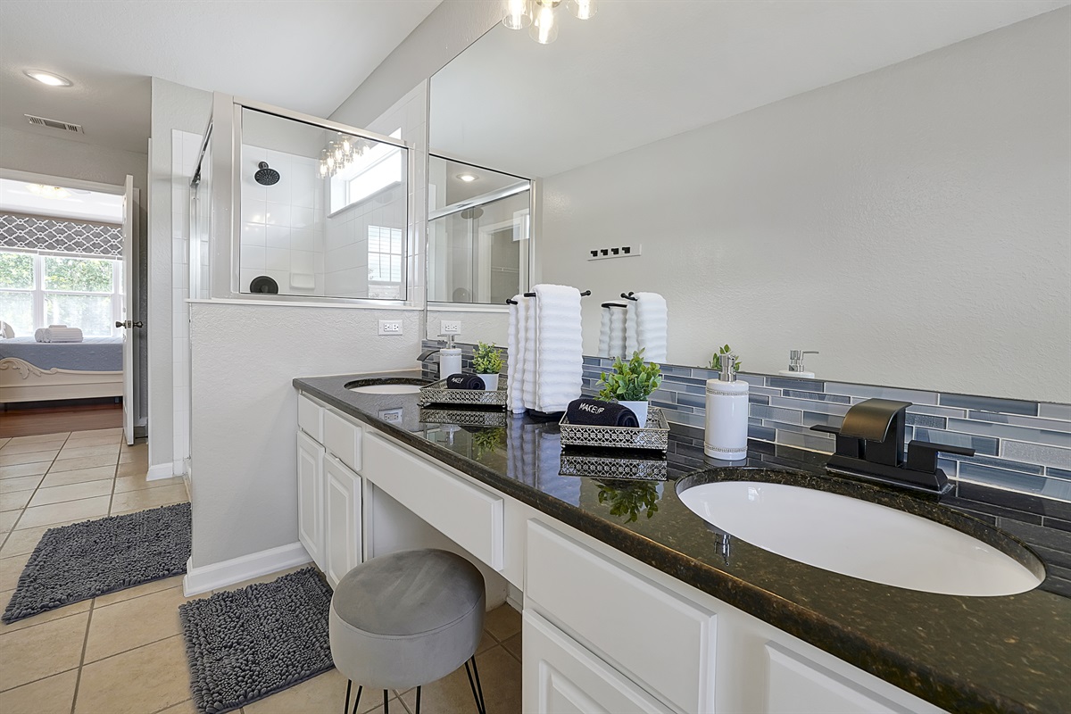 Clean and spacious, the primary bathroom features beautiful blue tile backsplash framing an oversized mirror above the double vanity. 