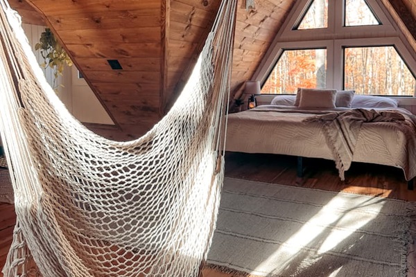 Adding a playful touch, a hammock is ingeniously built into the floor, perfect for lounging and soaking in the serene atmosphere. Nearby, a macrame swing hangs, providing a cozy nook to relax and sway gently while enjoying the tranquil forest view.