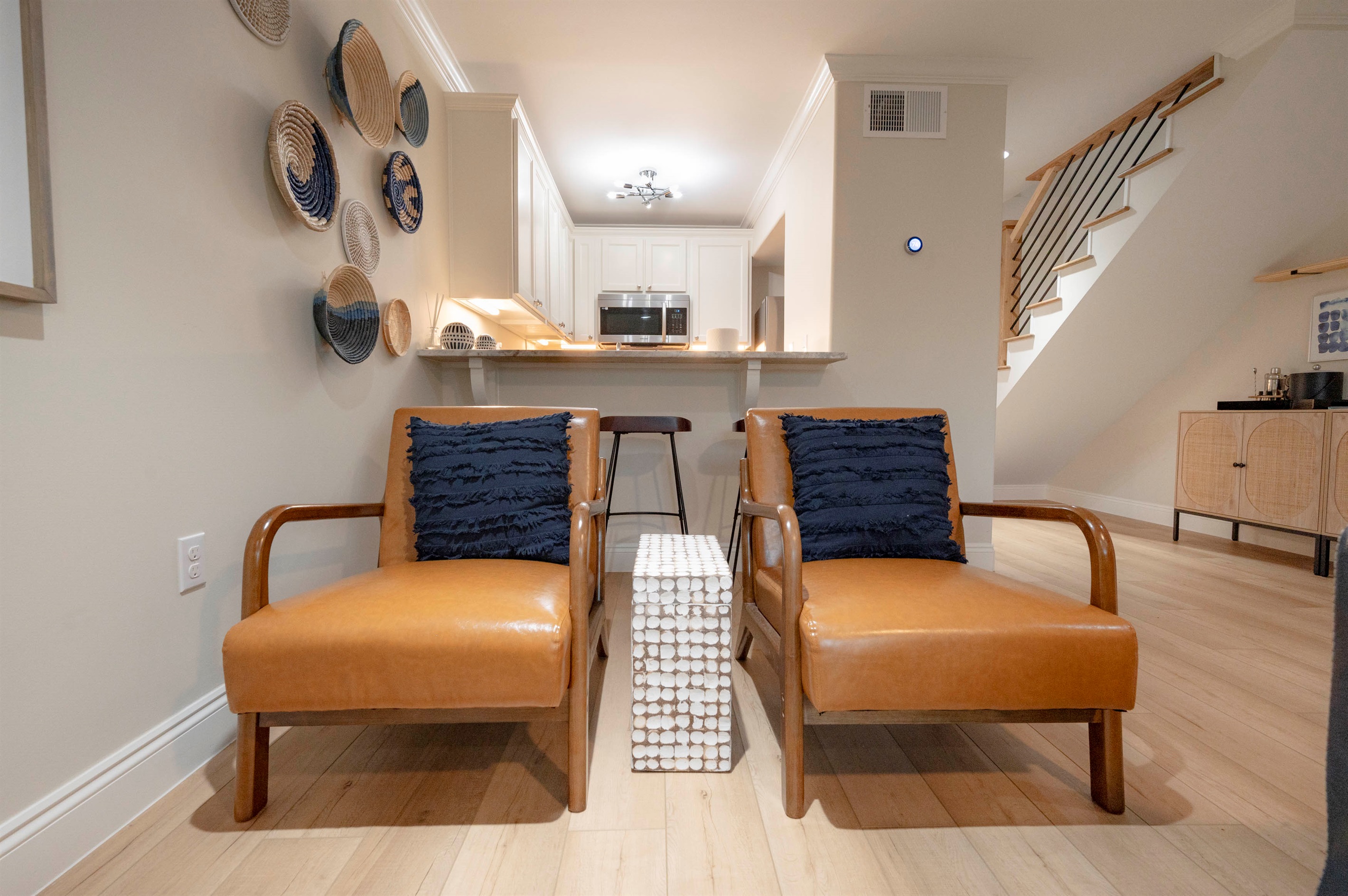 Relax in a modern living room with cozy leather chairs, stylish decor, and a sleek kitchen in the background.