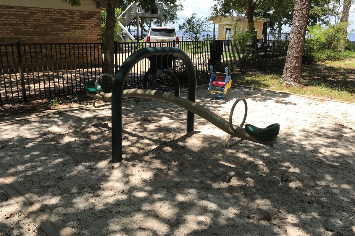 This shaded playground area offers a fun space for kids to play and explore while enjoying the fresh air. Surrounded by trees and soft sand, it’s a great spot for families to relax while little ones enjoy the seesaw and other play equipment.