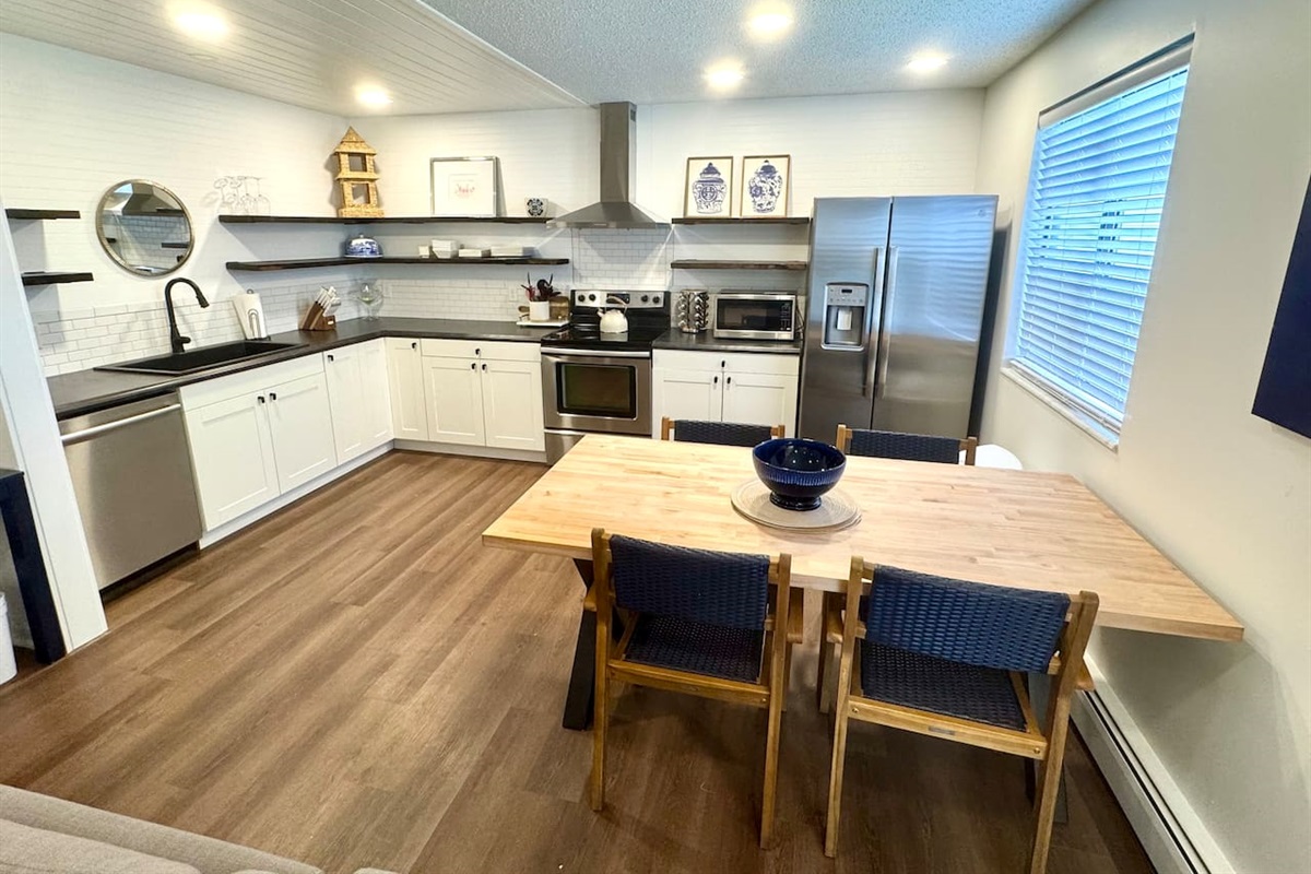 Modern kitchen with stainless steel appliances, open shelving, and a large butcher block dining table. Fully equipped for cooking, dining, and gathering. Bright, stylish, and functional—perfect for shared meals and memories