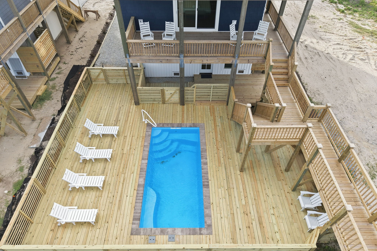 Aerial view of oceanfront pool deck with in-ground pool, lounge chairs, and multi-level wraparound decking with dune and beach surroundings