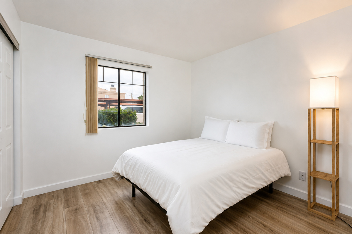 Simple queen bedroom with fresh white bedding, wood-look floors, closet space, and a floor lamp by the bed.