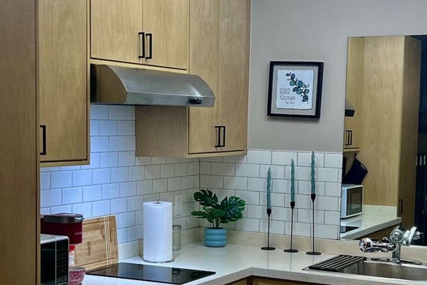 Kitchenette corner with wood cabinets, cooktop, sink, and space for simple meals.
