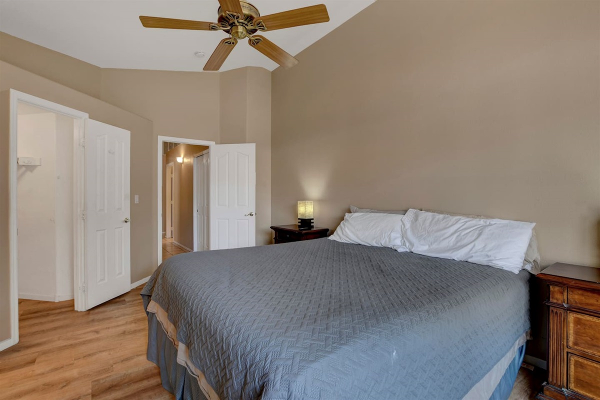 Serene king bedroom with vaulted ceiling, fan, and wood floors
