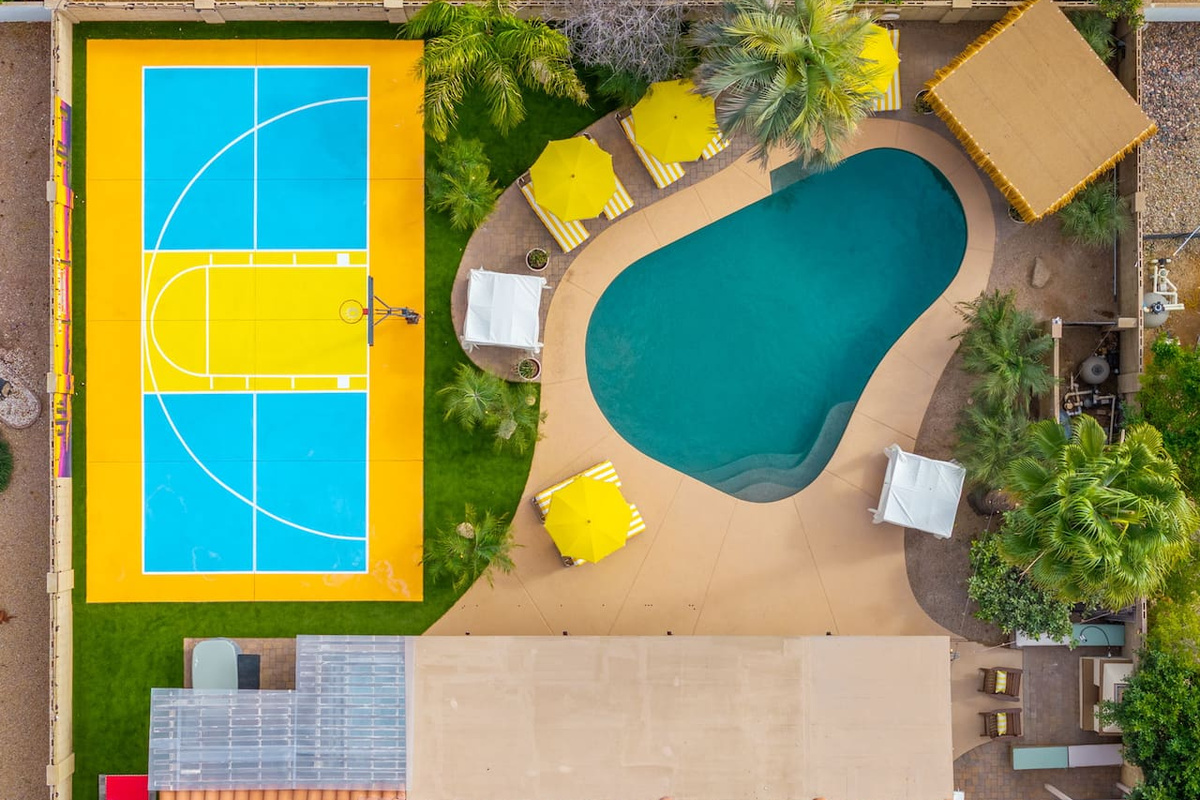 Overhead view of pool and sports court with yellow umbrellas and green landscaping—compact yet complete recreation space for guests.