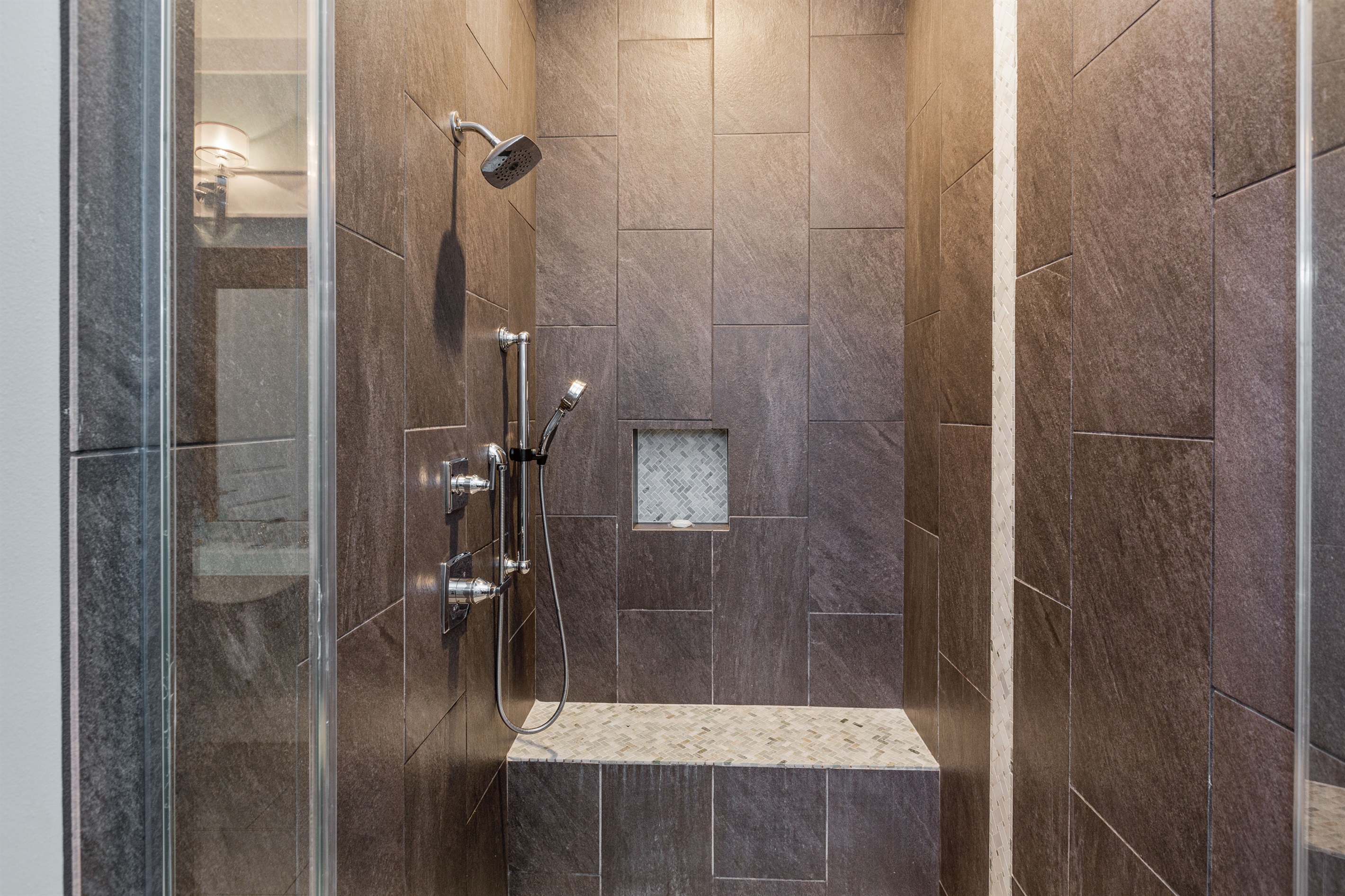 Luxurious oversized shower allows for wheelchair access and has both a stationary shower head as well as handheld shower features.