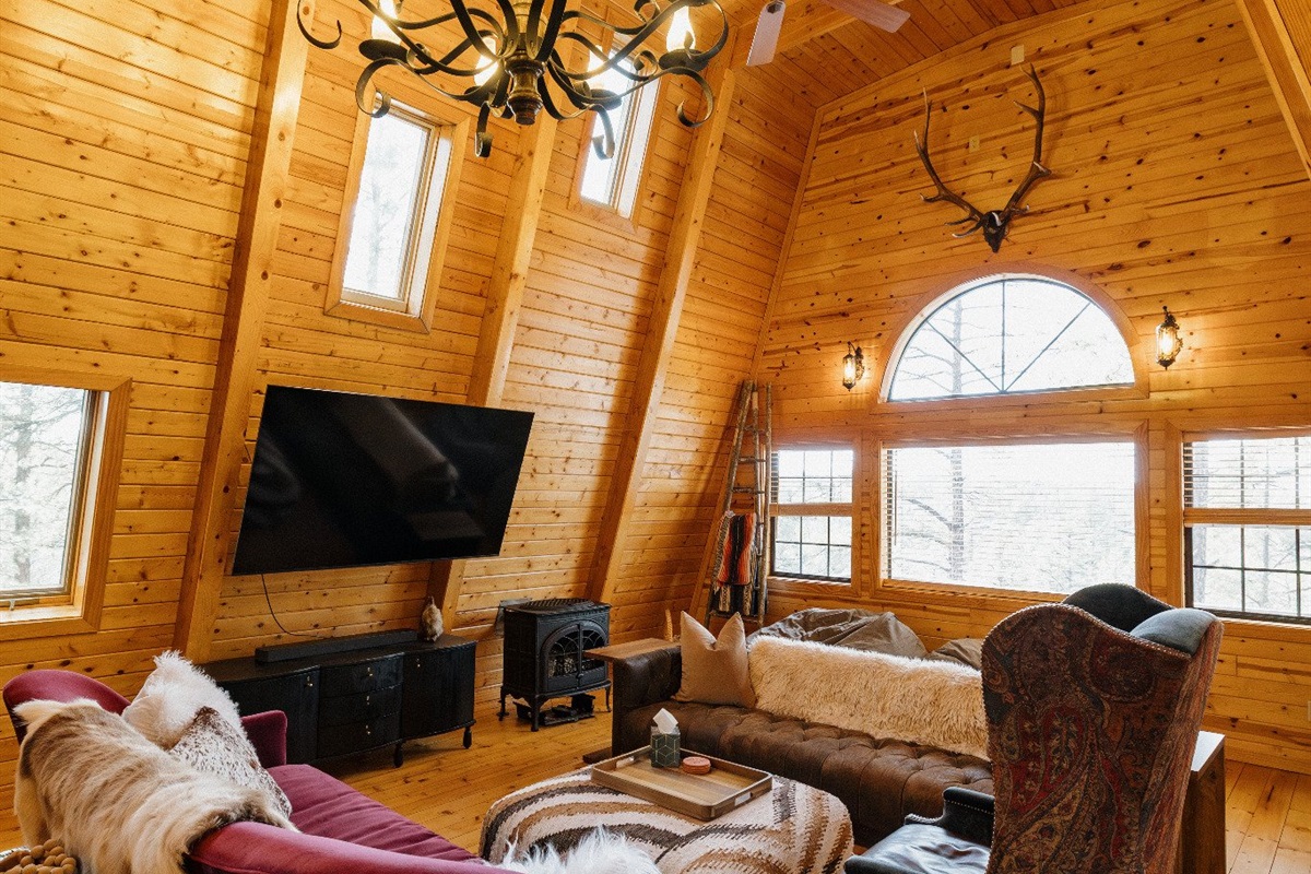 Light-filled A-frame living room with vaulted wood ceilings, eclectic seating, and cozy gathering spaces—perfect for lounging, game nights, and slow mornings in a warm, character-filled White Mountains cabin.