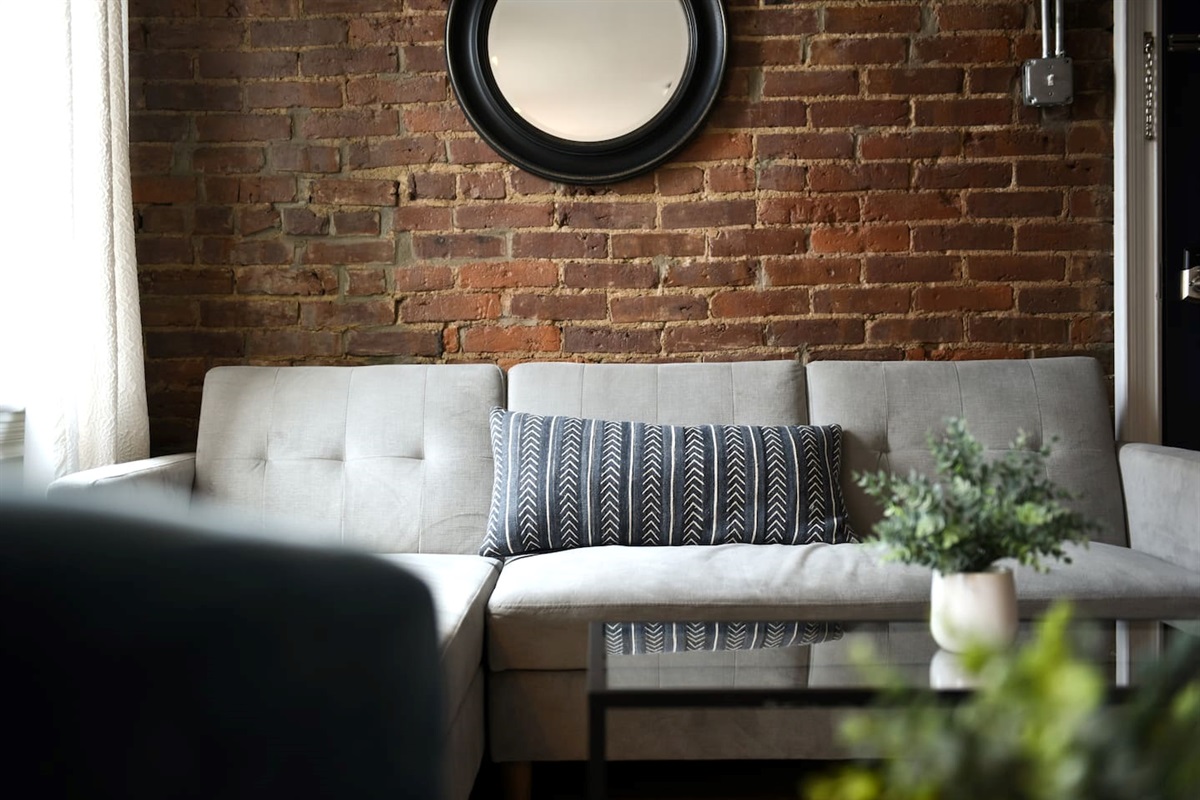 Lounge in a tastefully designed living room with a brick accent wall, large windows, and a mix of chic furniture for the ultimate cozy yet refined vibe.