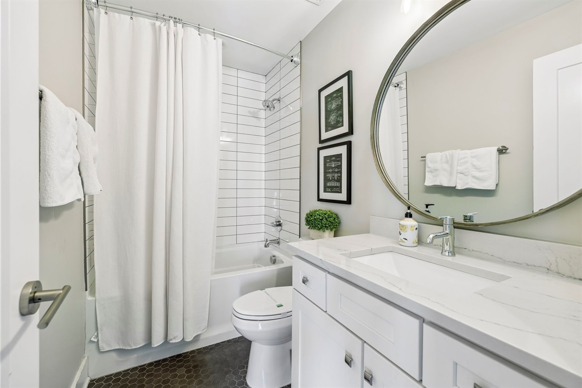 Subway tiled shower and tub combo behind a soft white curtain for a clean, classic look - Bright vanity with quartz counter & chrome fixtures offers style & functionality - Pops of color from fresh tulips and hex tile floor add personality and warmth