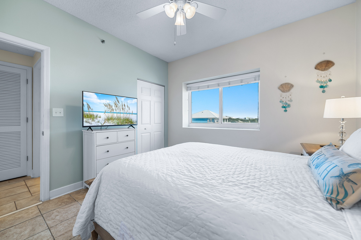 This well-appointed Guest bedroom features a Queen-size bed with a decorative headboard, crisp white bedding, matching nightstands with lamps, and tile flooring for easy maintenance.