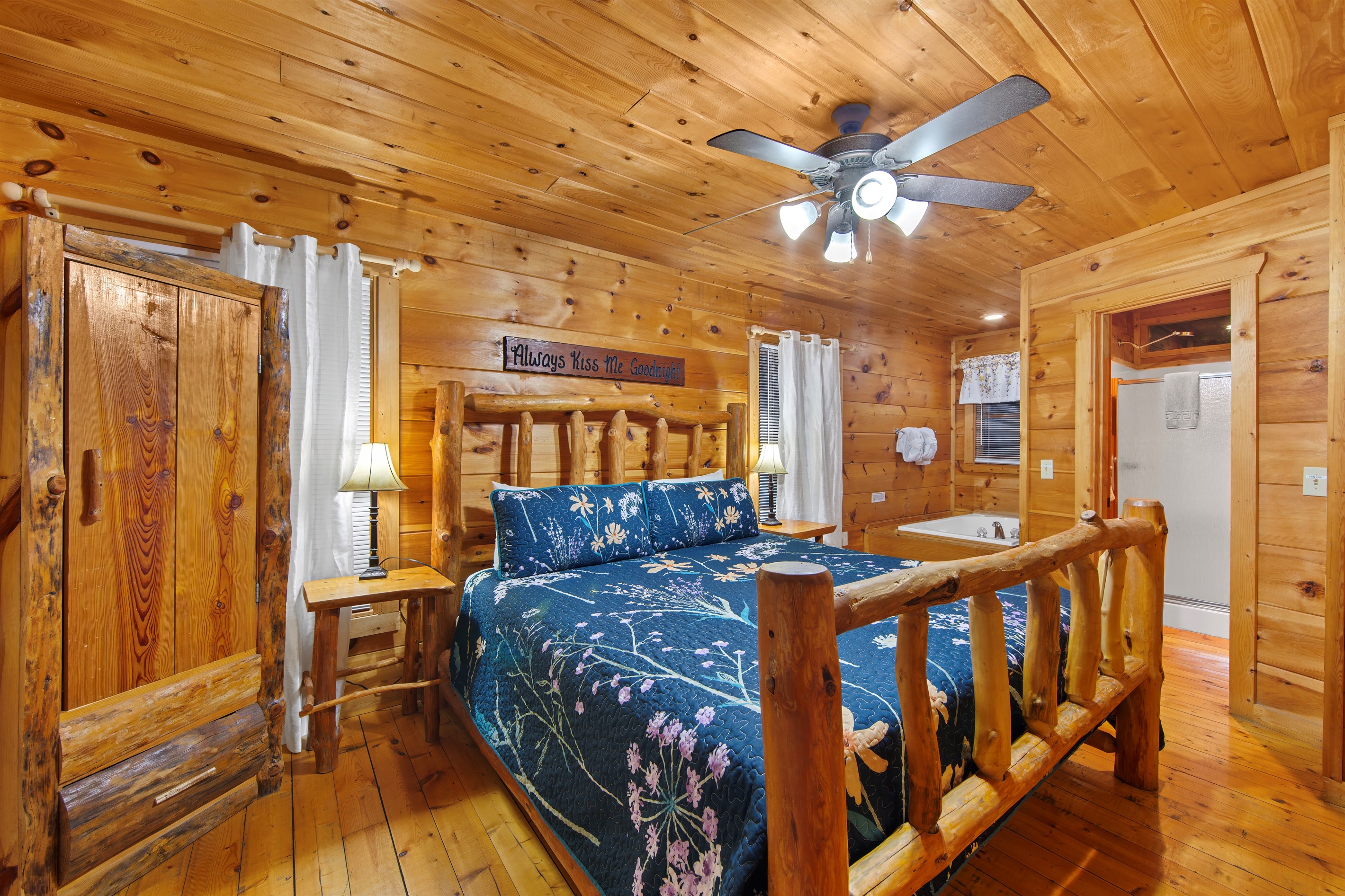 A tranquil cabin bedroom with a spacious log bed, vibrant blue bedding, and wood-paneled walls. The adjacent jetted tub adds a touch of luxury to this rustic haven.